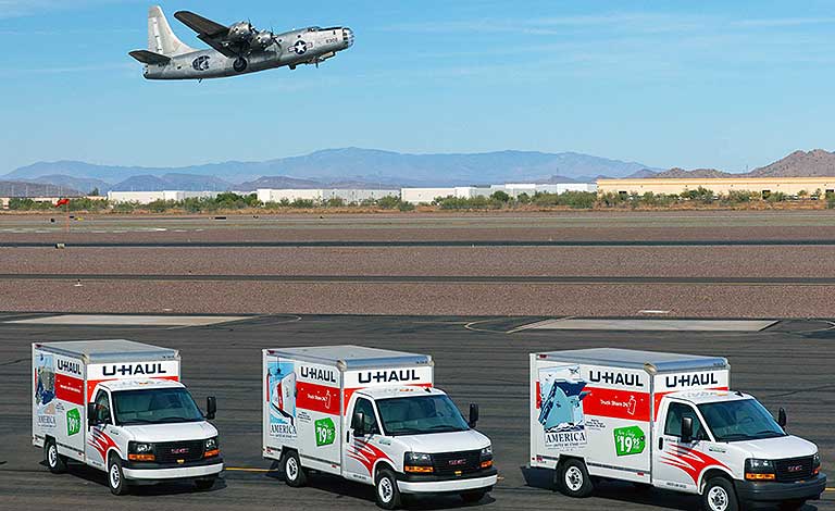 U-Haul Trucks parked next to an air field as a WWII-era Bomber takes flight