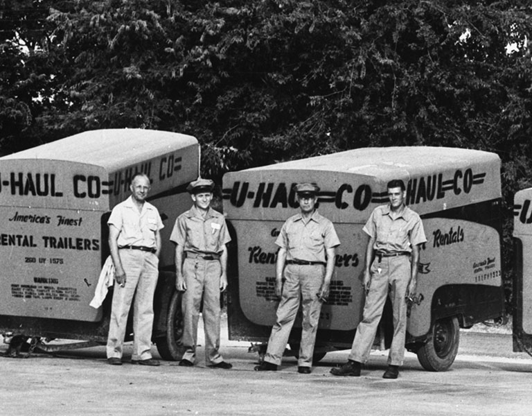 4 U-Haul employees standing in front of U-Haul trailers