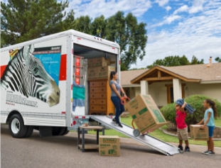 A woman and 2 children loading boxes into a U-Haul Truck