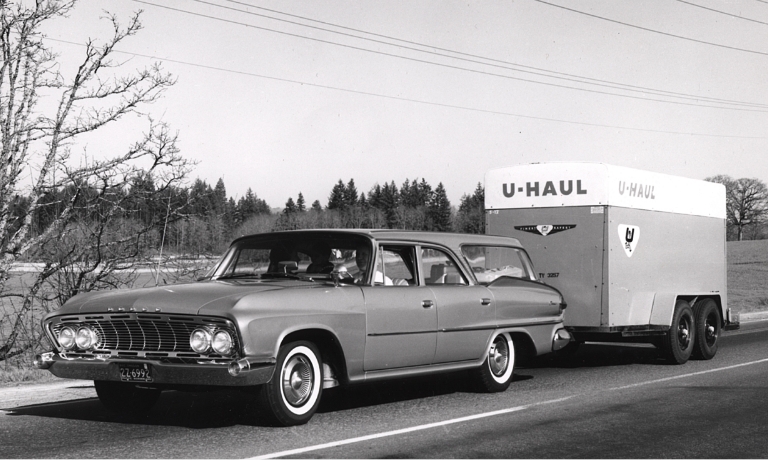 A vintage station wagon towing a U-Haul trailer