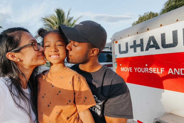 A couple and a child standing next to a U-Haul rental truck