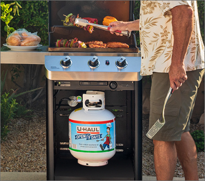 A propane grill with the top open, cooking meats and vegetables