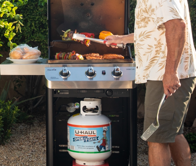 A propane grill with the top open, cooking meats and vegetables