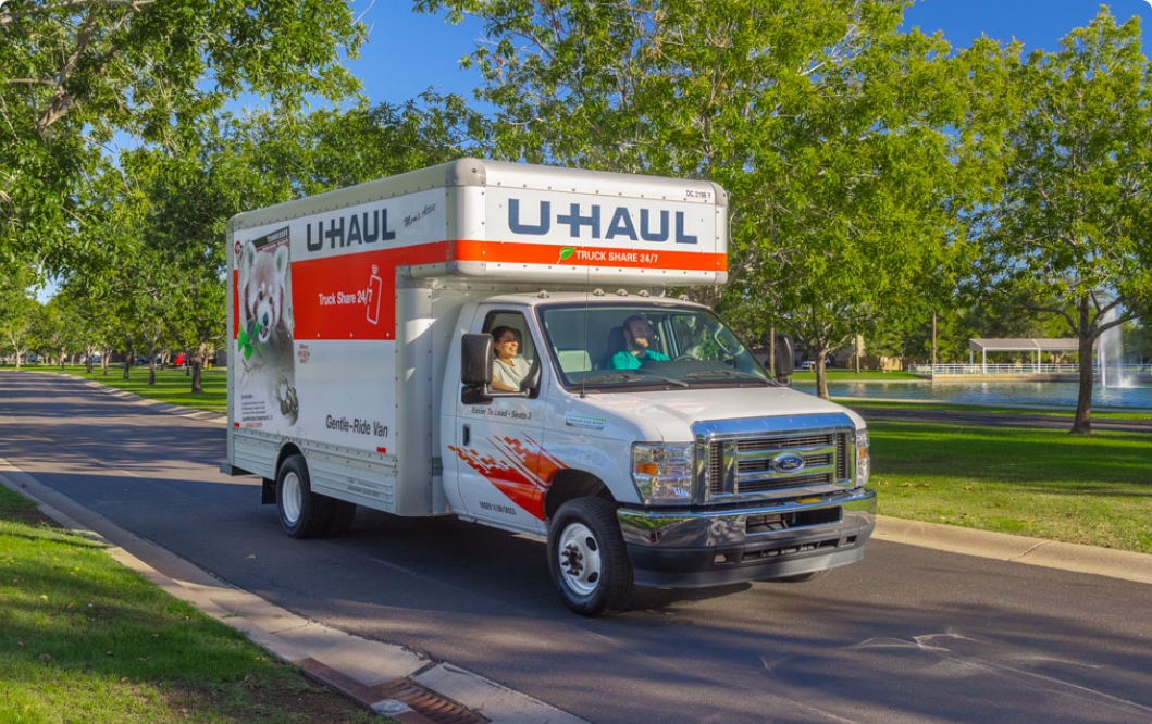 A couple in a U-Haul Truck driving along a street lined with trees