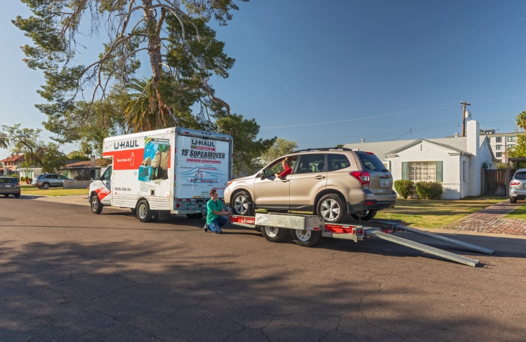 A U-Haul truck with a car carrier parked in front of a home