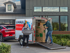A couple unloading a U-Haul cargo trailer in their driveway.