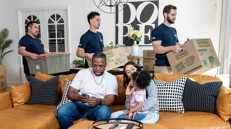 Moving helpers loading items into a family's home while the family sits on a couch