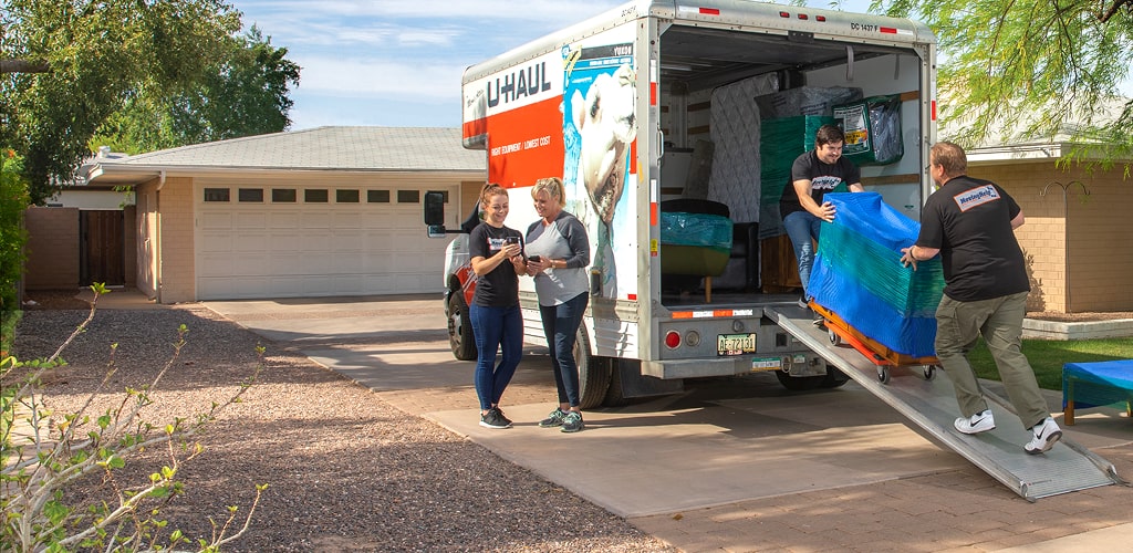 Moving Help® Service Providers loading a large dresser on a dolly into a U-Haul moving truck.