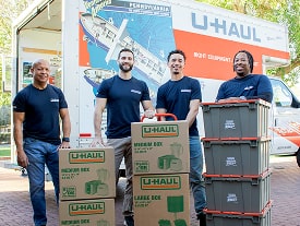 A group of Moving Helpers with loaded boxes standing in front of a U-Haul moving truck
