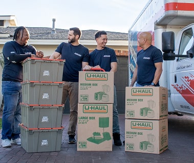 A group of Moving helpers with loaded boxes standing next to a U-Haul moving truck