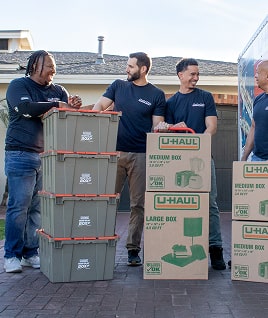 Group of Moving helpers with loaded boxes standing next to a U-Haul moving truck
