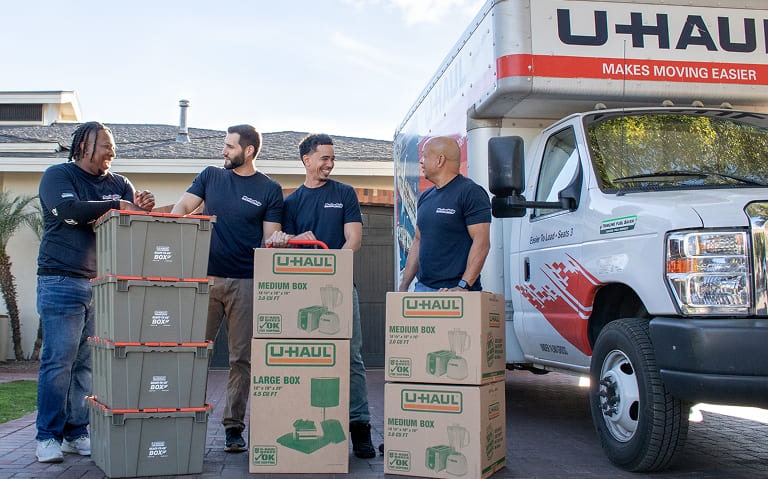 Group of Moving helpers with loaded boxes standing next to a U-Haul moving truck