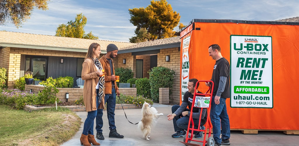 A couple standing in their driveway with Moving Helpers, one is petting their dog.